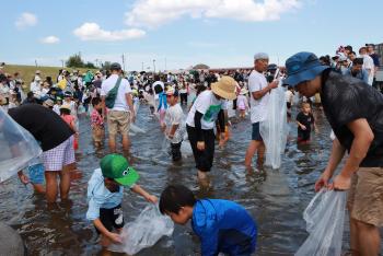 多くの家族連れが、浅い水に足をつけ、イワナのつかみ取りをしている写真