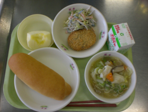 高岡コロッケの日の給食の写真。コッペパン、汁物、コロッケ、野菜、リンゴ、牛乳がある。