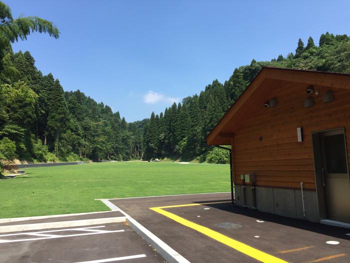 遠景に森林を臨む芝生の広場と建物の写真