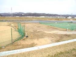 茶色い砂が広がっている地面に緑色のフェンスとテニスコートが設置されている写真