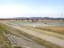 雑草が生えている堤防に手前に階段が設置され、奥に赤い橋が見える写真