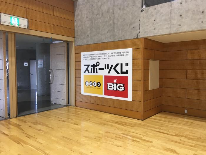 体育館の入り口付近の壁にスポーツくじのポスターが貼られた写真
