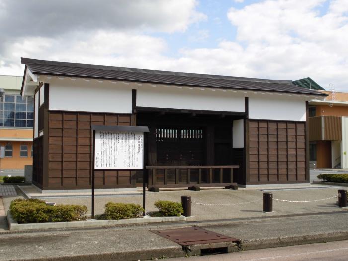 戸出御旅屋の門の写真。建物の前には戸出御旅屋の門の説明をした看板が立っている。