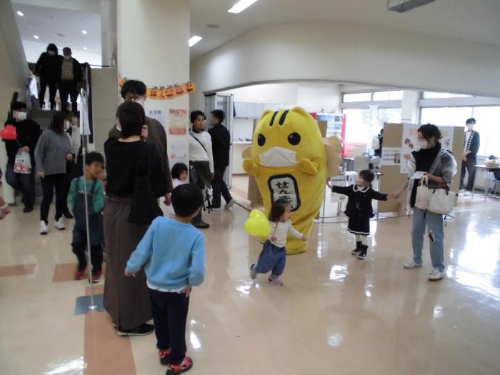 模擬投票の行われているスペースの外側でめいすいくんが子供たちと遊んでいる様子の写真