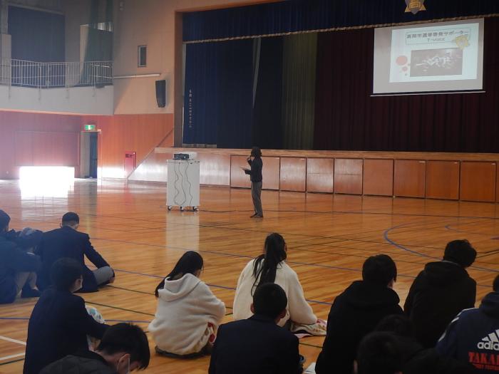 高岡第一高等学校の体育館で生徒たちにT-voiceの活動紹介をしているT-voiceメンバーの写真