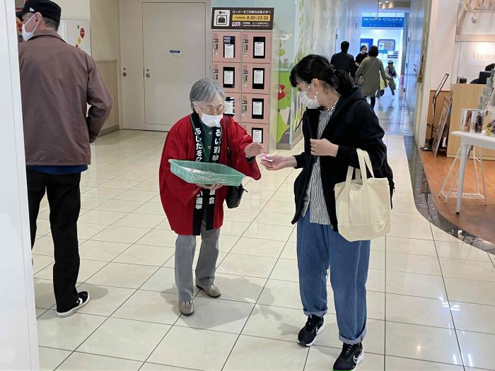街頭啓発で絆創膏を配布している女性とその絆創膏を貰おうとしている女性の写真