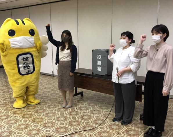 右手をあげているめいすい君と3人の女性の写真