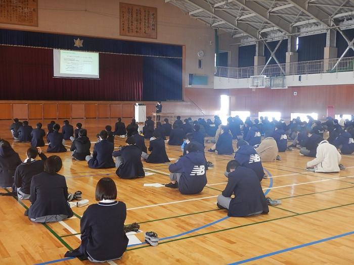 選挙啓発出前講座で体育館の床に座って講義を聞いている高岡第一高等学校の生徒たちの写真