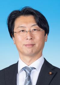 黒のスーツに縞模様の入った灰色のネクタイを着け眼鏡をかけた男性の写真