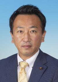 薄い線の入った紺のスーツにベージュ色のネクタイを着けた男性の写真