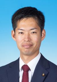 黒のスーツに暗い赤色のネクタイを着けた男性の写真