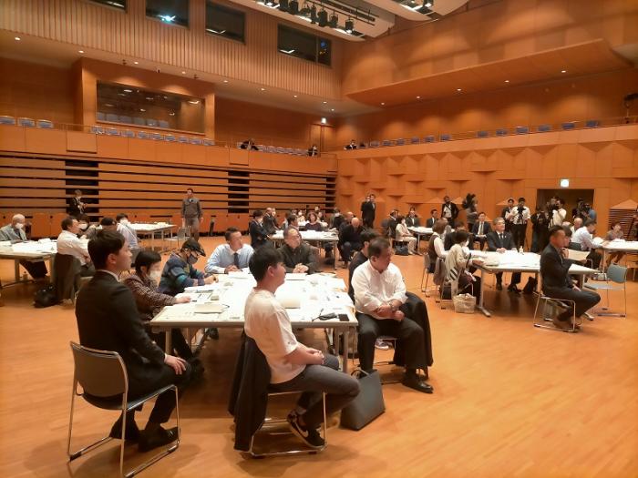 広いホールでいくつかテーブルにそれぞれ囲うように座る人々の写真