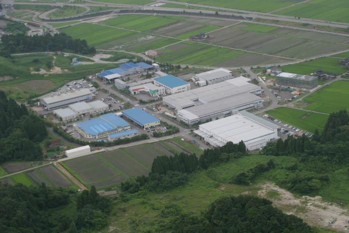 木や田んぼに囲まれている中に建物が並んでいる岩坪工業団地の様子を上空から撮影した写真