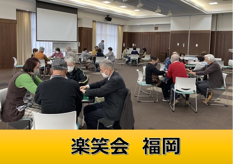 楽笑会福岡と書かれたタイトル書きと、複数の男女が幾つかあるテーブルを囲んで、ゲームのようなものを行っている様子の写真