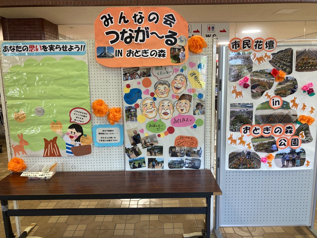 「みんなの会 つなが～る in おとぎの森」と書かれた紙が貼ってあり、写真やイラスト、参加者のコメントが掲載されている展示板