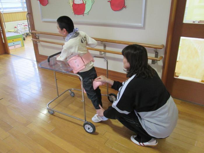 歩行器に掴まる子供とその子供の足を支える女性の写真