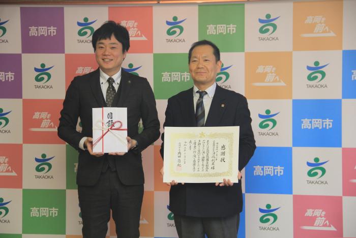 スーツを着た2人の男性が立って目録と感謝状を掲げている株式会社 アーキジオ様の写真