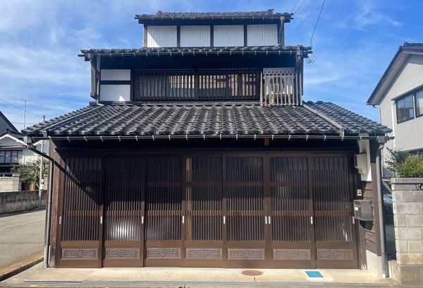 1階部分の入り口に設えられた焦げ茶色の格子意匠の引き戸と瓦屋根が特徴的な2階建ての建物の写真