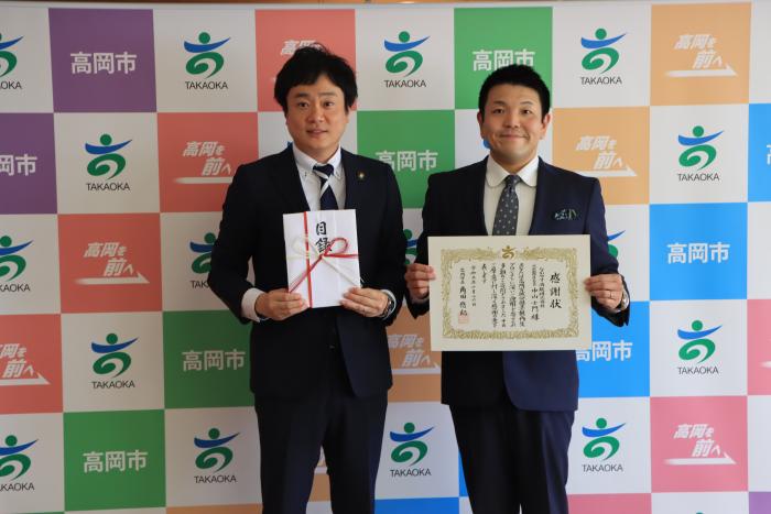スーツを着た2人の男性が立って目録と感謝状を掲げているなかやす酒販様の写真