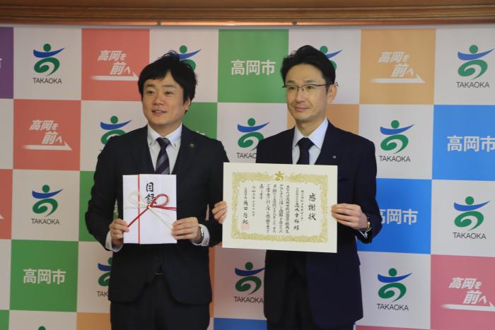 スーツを着た2人の男性が立って目録と感謝状を掲げている株式会社タカギセイコー様の写真