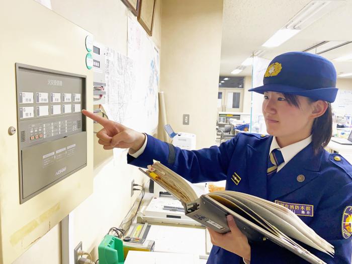 火災受信機を右手で指差ししてチェックする藤井柚朱消防士(先輩消防士藤井柚朱からのメッセージへのリンク)
