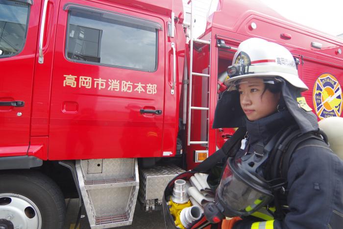 消防車の前で防火服に身を包み、真剣なまなざしで前を見ている竹山消防士の写真