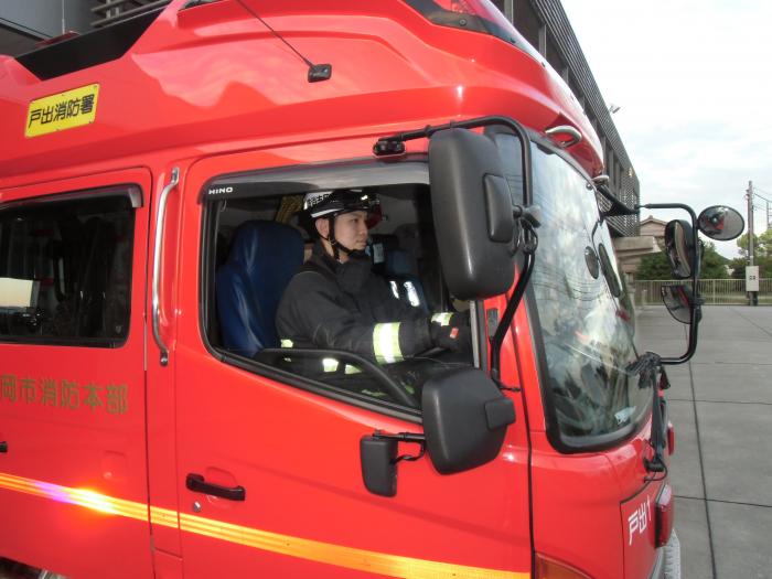 ヘルメットをかぶり消防車の運転席に座りハンドルを握る森田佳守馬消防副士長(先輩消防士森田佳守馬からのメッセージへのリンク)
