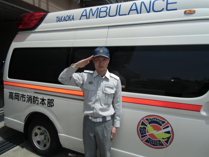 停車中の高岡市の救急車を背景に敬礼する田中貴大消防副士長(先輩消防士田中貴大からのメッセージへのリンク)