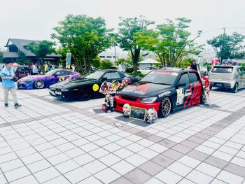 手前に赤と黒のコントラストの車があり、その向こうに黒の車や紫の車が見える写真
