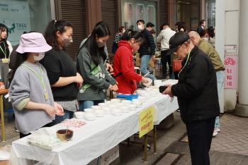 テーブルに並べられた小さな容器に入った料理を買おうとする年配の男性の写真