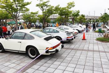 手前に白いポルシェが置かれ、その向こうにもさらに高級車が何台も並んでいる写真