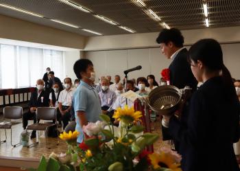 花で飾られた会場で、表彰を受ける男子児童の写真
