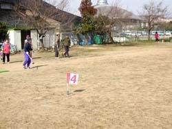 運動広場内に立てられた「4」と書かれた旗と、スティックを手に歩く大人達の写真