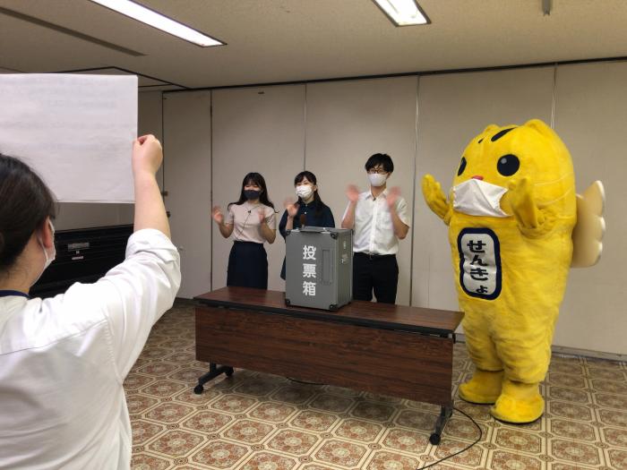 カメラの前で手を振っているめいすい君とT-voiceメンバーの写真