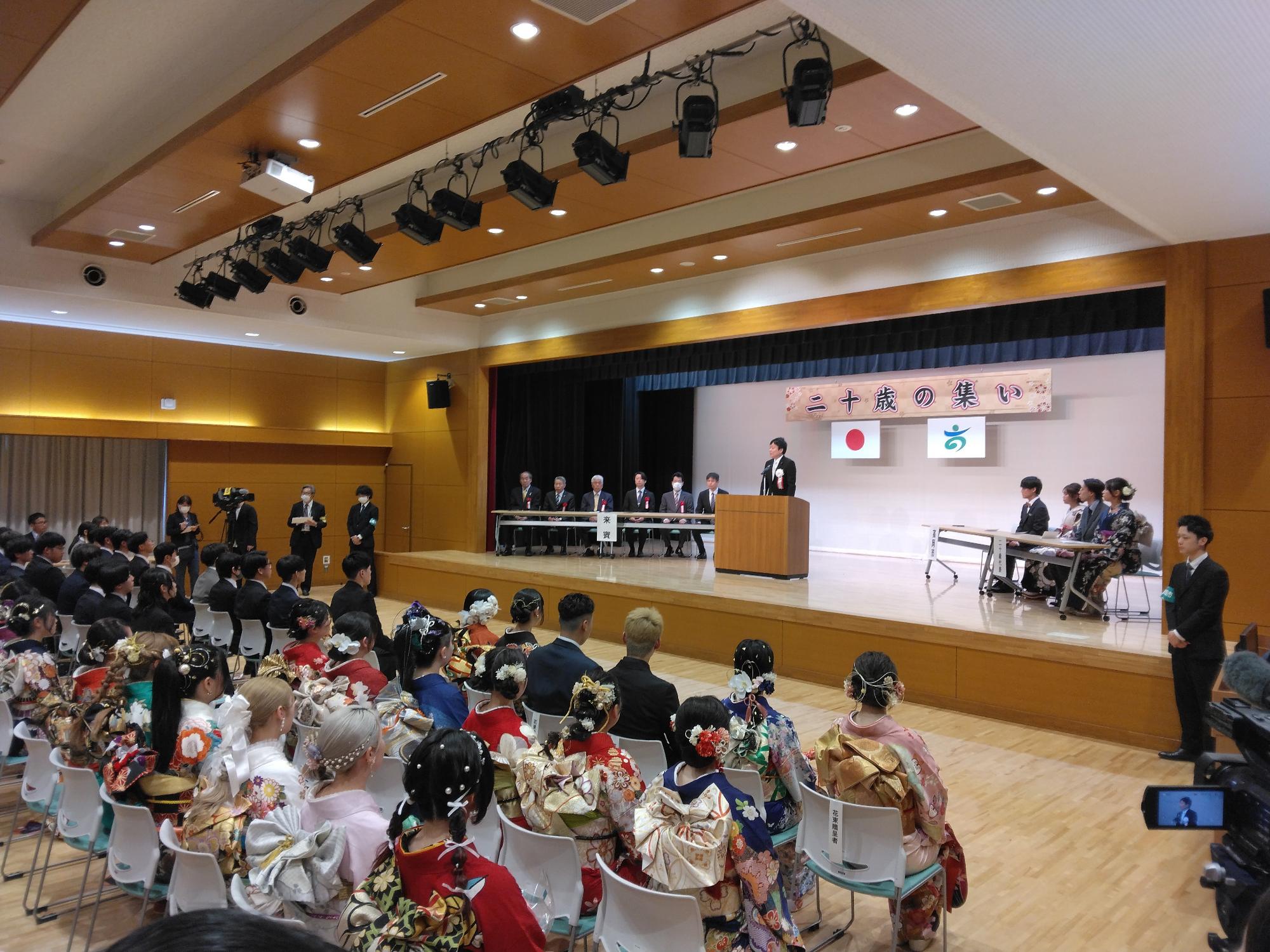 二十歳のつどいにて大勢の晴れ姿の参加者の前で祝辞を述べる市長